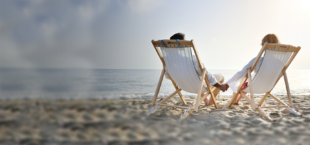 Ein Paar sitzt am Strand im Liegstuhl und schaut aufs Meer – Symbolbild für Auslandsreise-Krankenversicherung