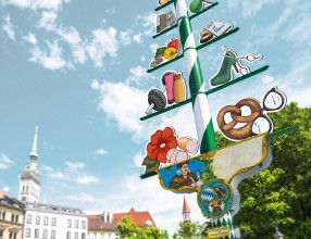 Bild von einem fiktiven Maibaum mit Darstellungen von verschiedenen Handwerken und Geschäften – Symbolbild für eine Sachversicherung für Firmenkunden