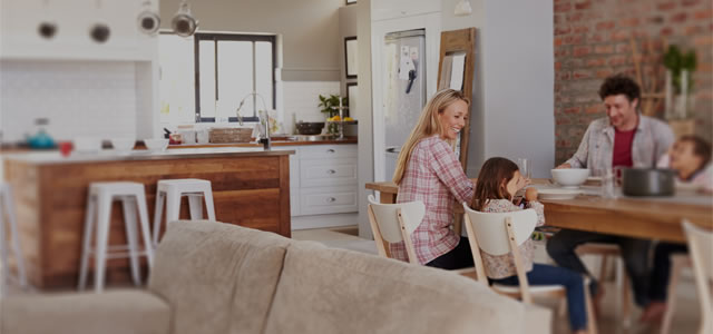 Familie sitzt gemeinsam beim Essen an einem Tisch in ihrem offenen Küche-Wohnbereich