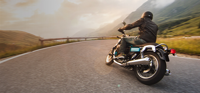 Mann, der in den Bergen Motorrad fährt – Symbolbild für eine Kfz-Versicherung für Motorradfahrer